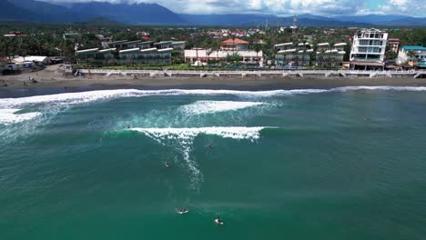 a dolly-out wide shot gracefully pulls back from the shore, revealing surfers riding the waves along the coastline, while beach houses are scattered across the sandy expanse.