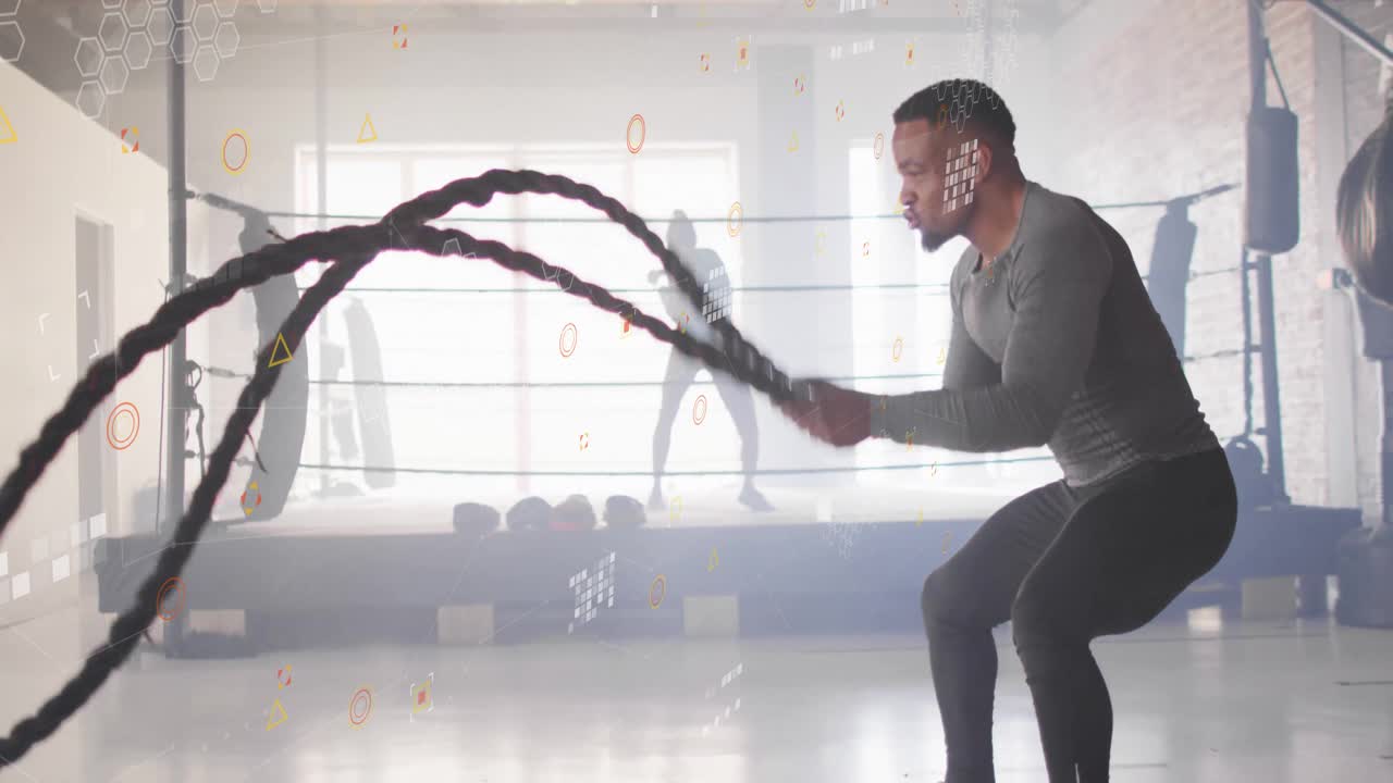 Homme accroupi tenant des cordes de combat, créant des vagues pour le fitness, tandis qu'une femme frappe un sac de boxe