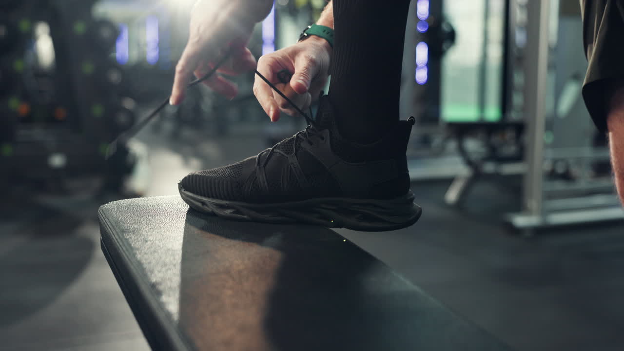 Man tying shoelaces on a bench in a gym