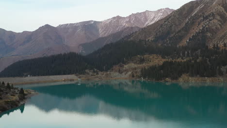 side drone footage of the turquoise colored lake water at big almaty lake and the trans-ili alatau mountains in kazakhstan