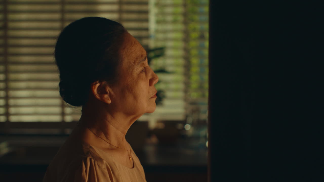 Old woman standing by the fridge, lost in thought before walking away in a quiet moment