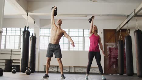 mujer y hombre caucásicos en forma trabajando con campanas en el gimnasio