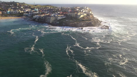 Aerial:-Tilt-up-from-the-ocean-whilst-moving-towards-the-peninsula-at-Bondi-Beach,-Australia