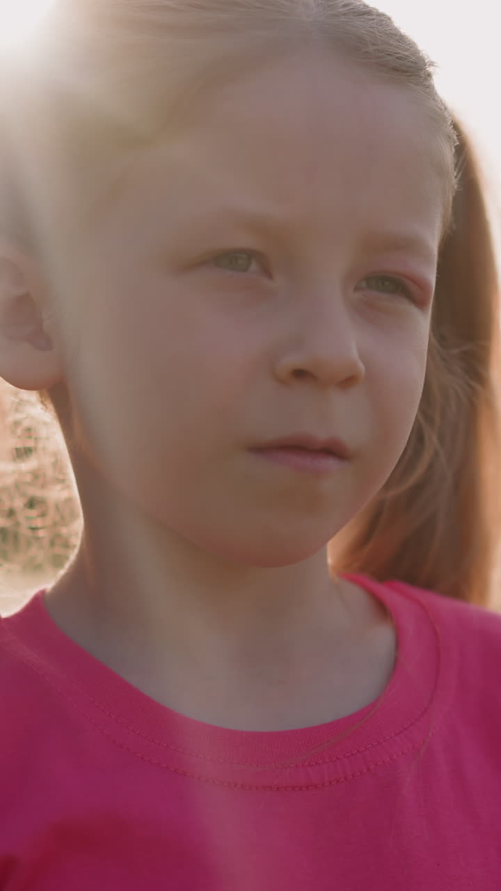 Unhappy little girl with swollen eyelid stands in green field at sunset closeup slow motion. Traumatic accident at promenade. Insect bite