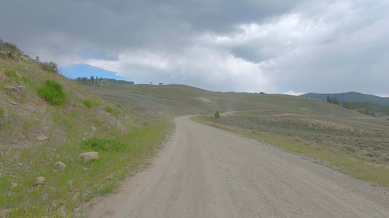 pov a través de la ventana trasera mientras conduce por un camino de ripio a través de un prado alpino en las montañas rocosas de colorado, estados unidos en un día nublado
