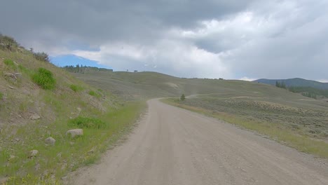 POV-thru-the-rear-window-while-driving-on-gravel-road-thru-an-alpine-meadow-in-the-Rocky-Mountains-of-Colorado,-USA-on-a-cloudy-day