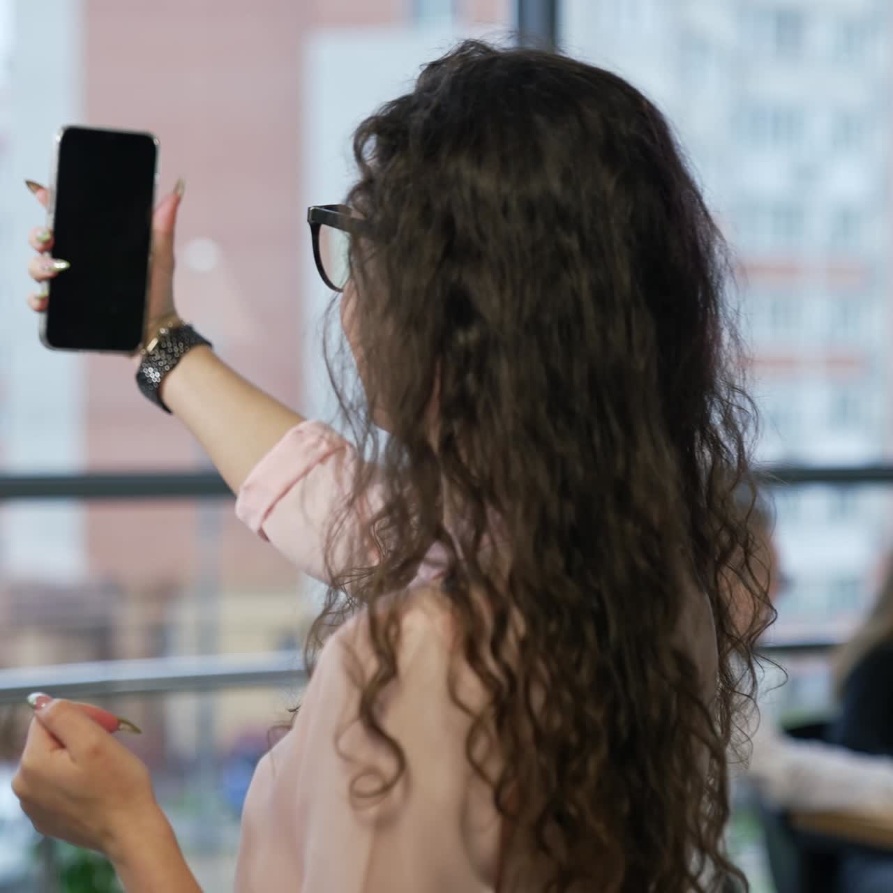 Attractive young woman takes selfie in office. Female employee shooting video on her mobile phone while turning around