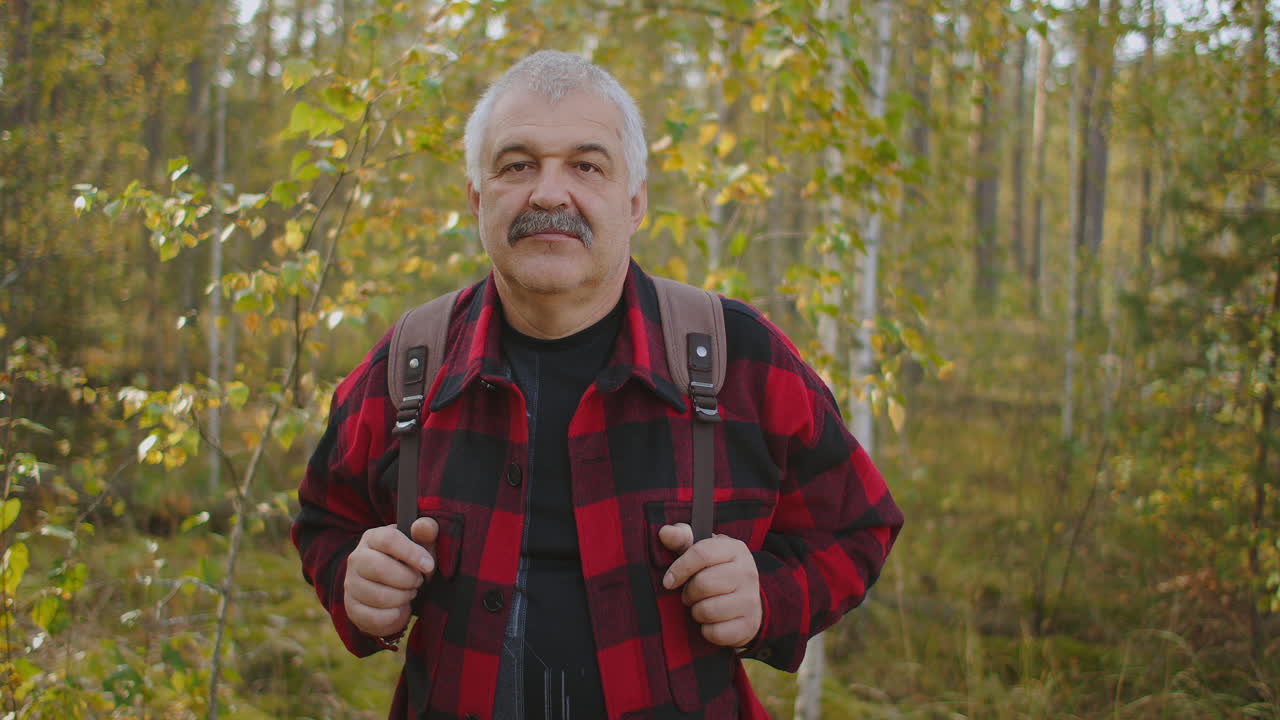 turista feliz en el bosque de otoño retrato medio durante el día hombre de cabello gris con bigote está sonriendo alegremente
