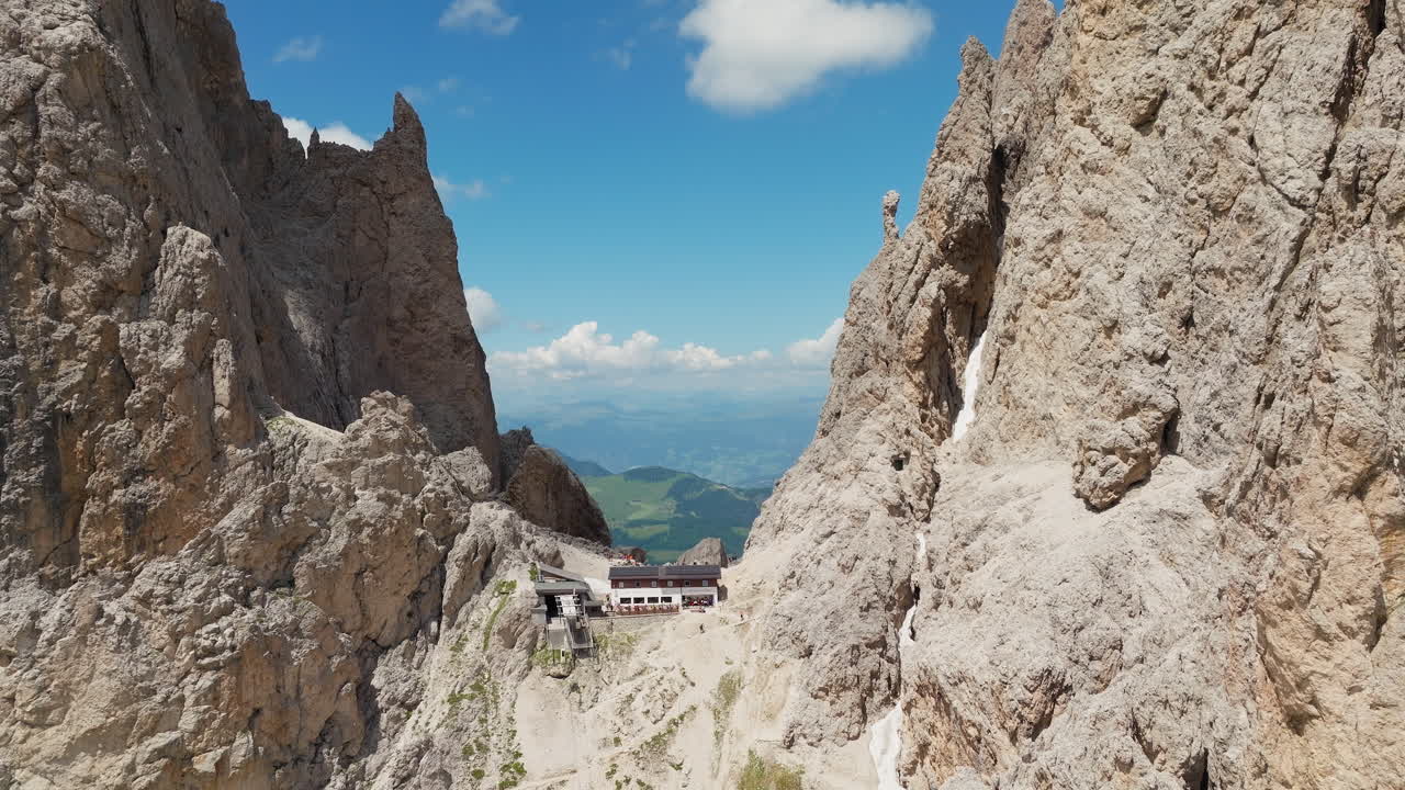 Backwards reveal drone shot of the iconic Toni Demetz Hut perched dramatically in the Forcella del Sassolungo, Dolomites, Italy