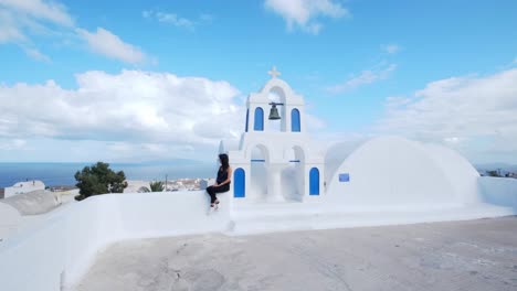 Girl-sitting-on-top-of-white-blue-church,-view-of-Aegean-sea
