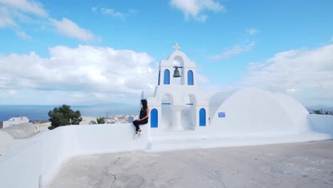 girl sitting on top of white-blue church, view of aegean sea