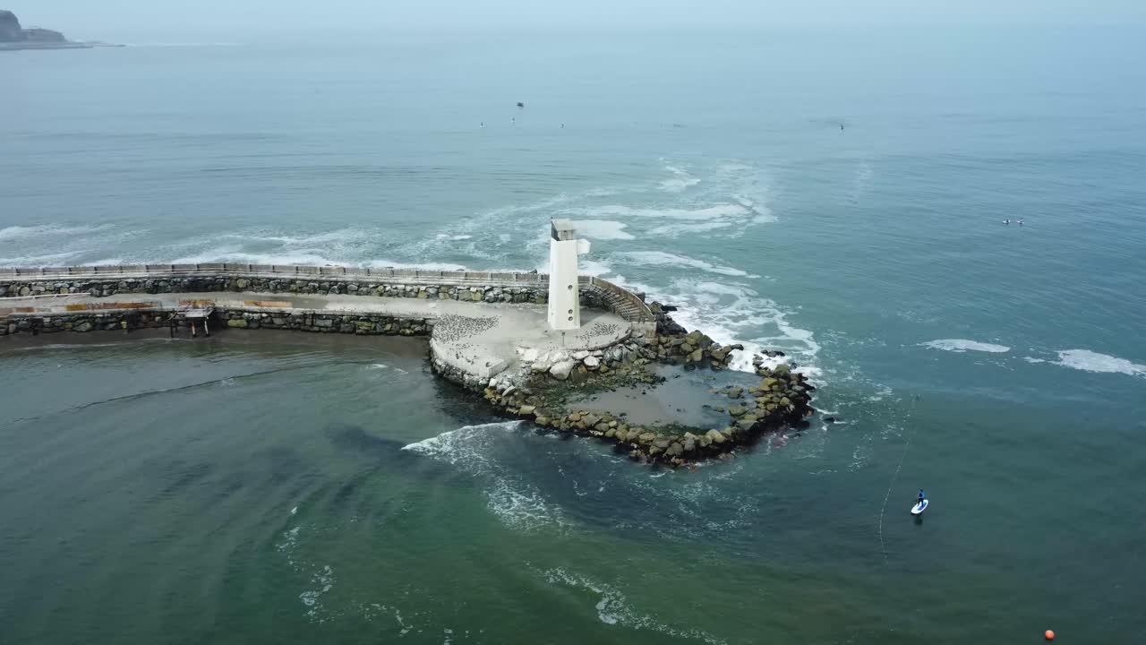 drone orbita alrededor de un pequeño faro blanco en el borde de un muelle rocoso