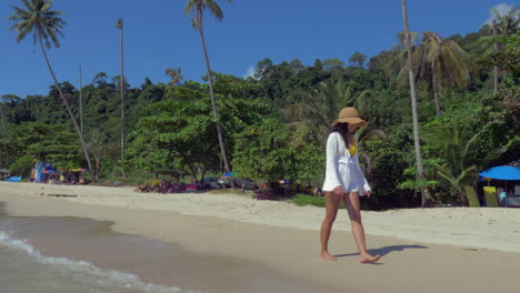 Zeitlupenaufnahme-Einer-Frau-In-Einem-Weißen-Kleid,-Die-An-Einem-Malerischen-Strand-Spaziert