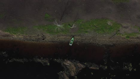 Vom-Himmel:-Drohnenaufnahmen-Zeigen-Ein-Am-Ufer-Vor-Anker-Liegendes-Fischerboot-Vor-Dem-Harmonischen-Hintergrund-Aus-Blau-Und-Grün,-Der-Durch-Vereinzelte-Umgestürzte-Wälder-Verstärkt-Wird