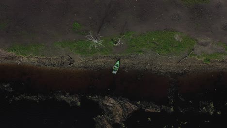 from the sky: drone footage reveals a fishing boat anchored on the shore, set against the harmonious backdrop of blue and green, enhanced by scattered fallen woods