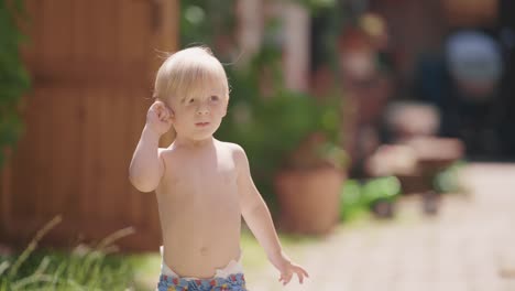 a little blonde-haired fair-skinned boy runs happily in the yard of the rural house