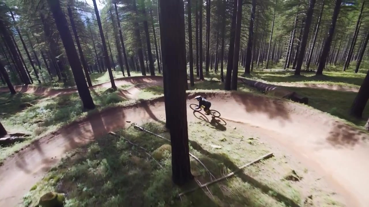 Hjälmförsedd förare i mörk utrustning går in i en berm, lutar sig och cyklar runt en pump track i tallskog, håller hastigheten.