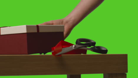 close up of man putting down gift wrapped presents in boxes decorated with ribbon on table shot against green screen