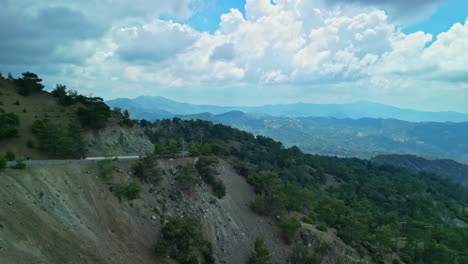 Eroded-dirt-cliff-side-road-in-front-of-panoramic-countryside-landscape,-aerial