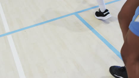 low section of diverse male basketball team training, stepping sideways at indoor court, slow motion