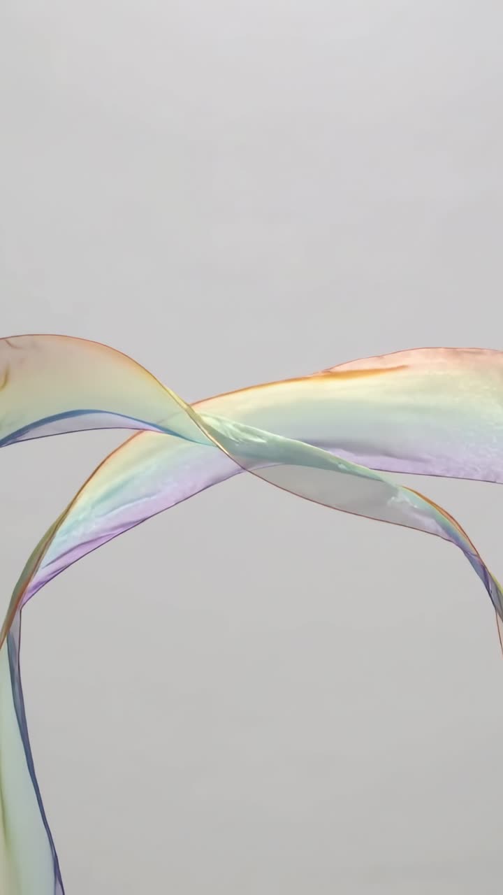 Vertical video: Waving iridescent ribbon crossing X and forming arcs in studio, showing color