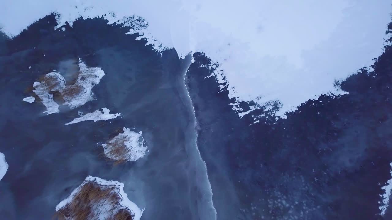 vista aérea de pájaro del lago congelado liepaja durante el invierno, hielo azul con grietas, islas secas de juncos amarillentos, día de invierno nublado, amplio disparo ascendente de drones