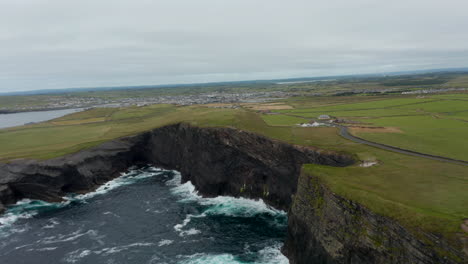 Toma-Aérea-Ascendente-De-Olas-ásperas-Rompiendo-En-Un-Alto-Acantilado-Rocoso.-Hermoso-Hito-Natural.-Vista-Panorámica-Del-Paisaje-Plano.-Paseo-Del-Acantilado-De-Kilkee,-Irlanda