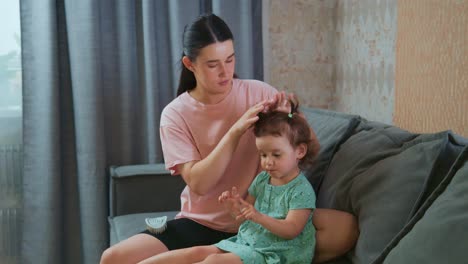 A Caring Moment: A Mother Gently Styles Her Daughter&#039;s Hair on a Cozy Couch, Creating Special Memories in a Warm and Loving Environment