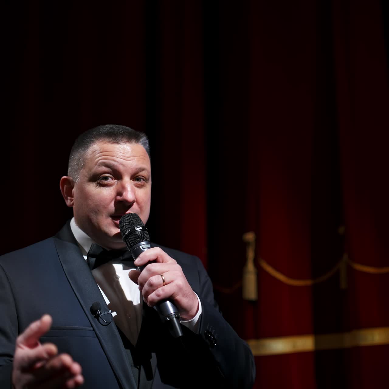 Experienced host with a microphone. Positive man in gray costume standing on theatrical stage and talking on camera. Lockdown during pandemic