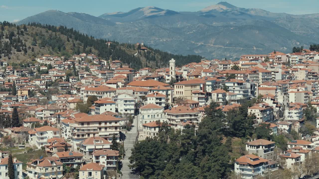 Ripresa orbitale con drone, sopra un villaggio su una collina verde in Europa, tetti rossi, piccole case, tempo soleggiato, montagne innevate, Grecia, video 4K