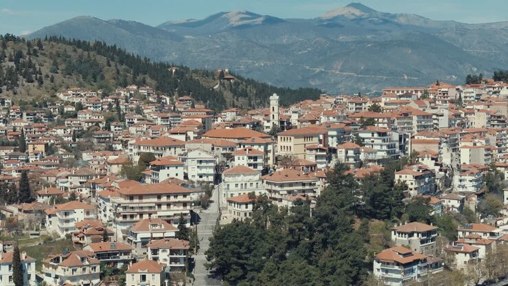 Ripresa orbitale con drone, sopra un villaggio su una collina verde in Europa, tetti rossi, piccole case, tempo soleggiato, montagne innevate, Grecia, video 4K