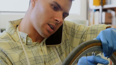 Man-talking-on-mobile-phone-while-repairing-bicycle-4k