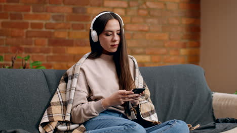 woman relaxing on couch with headphones and smartphone