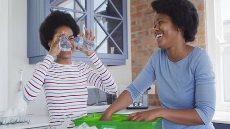 happy african american mother and daughter recycling together in kitchen