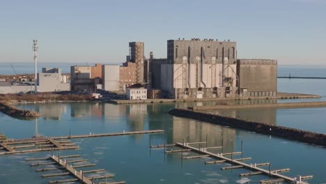 Industrial-waterfront-with-grain-elevators-at-Port-Colborne,-calm-water,-clear-sky,-no-people,-daylight,-aerial-view