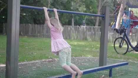 wide shot of a 4 years old girl in slow motion in a playground who is swinging on a bar and then jumping