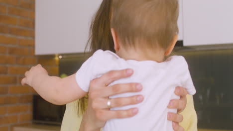 Close-Up-View-Of-Woman-Laying-Her-Baby-On-The-Kitchen-Counter-While-Working-On-The-Laptop