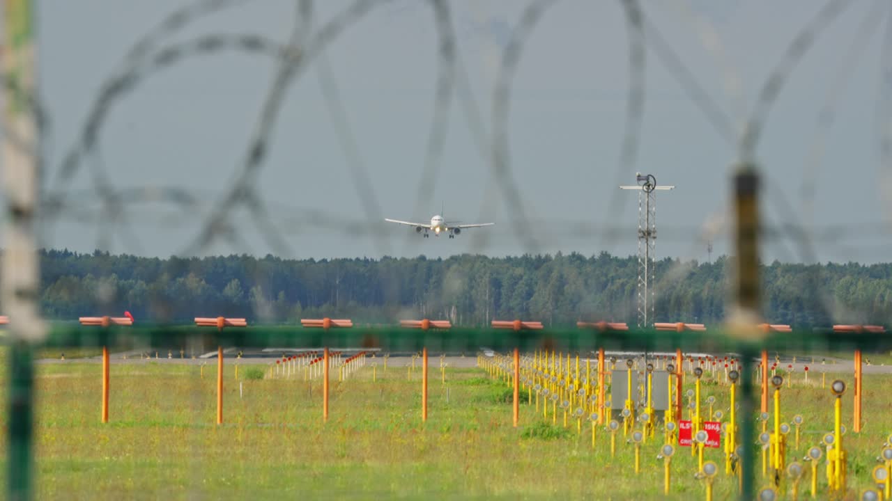 Passenger plane touching down on runway with barbed wire fence in foreground, frontal view
