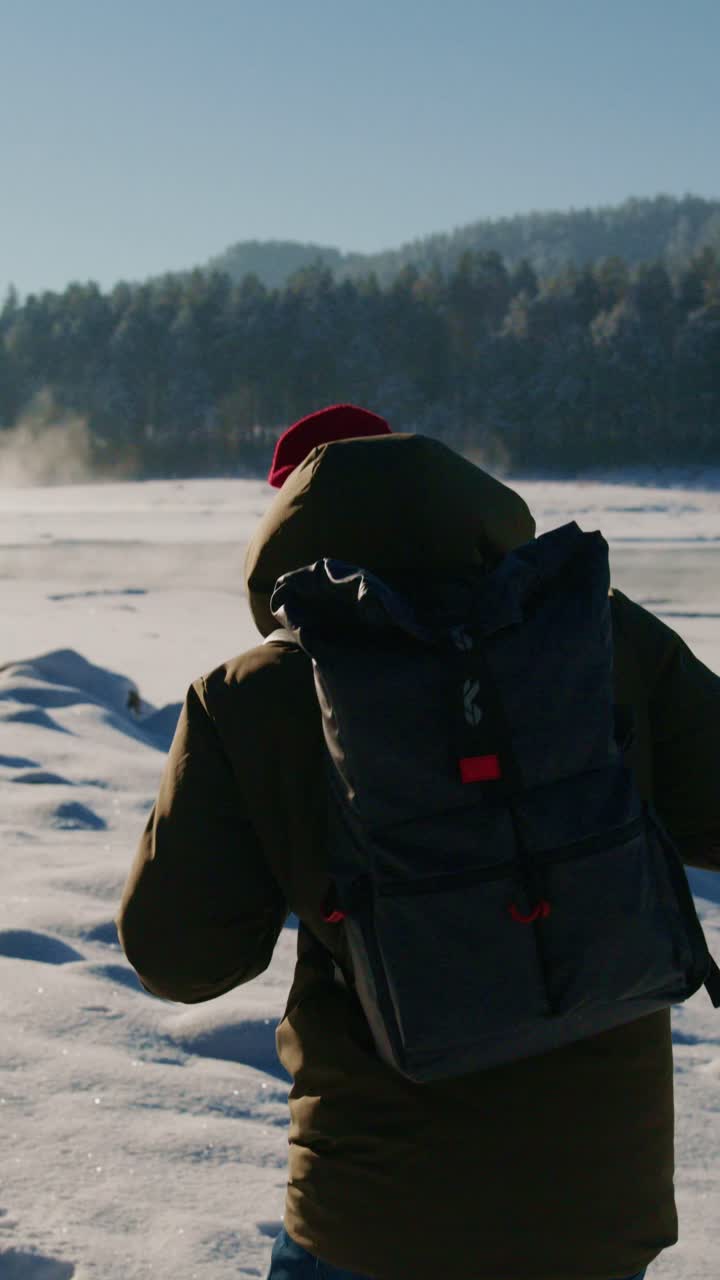 Man trekking through snow-covered landscape wearing warm clothing and backpack in winter