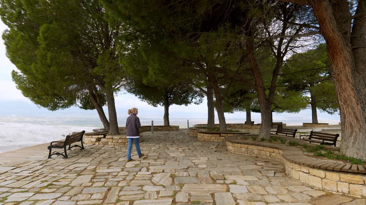Female wanders in quiet tree shaded viewpoint area with crazy stone paving
