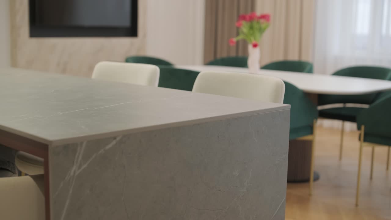 Close-up of a marble table in a stylish interior with plush green chairs and a bouquet of flowers in the softly blurred background