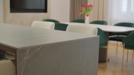 close-up of a marble table in a stylish interior with plush green chairs and a bouquet of flowers in the softly blurred background