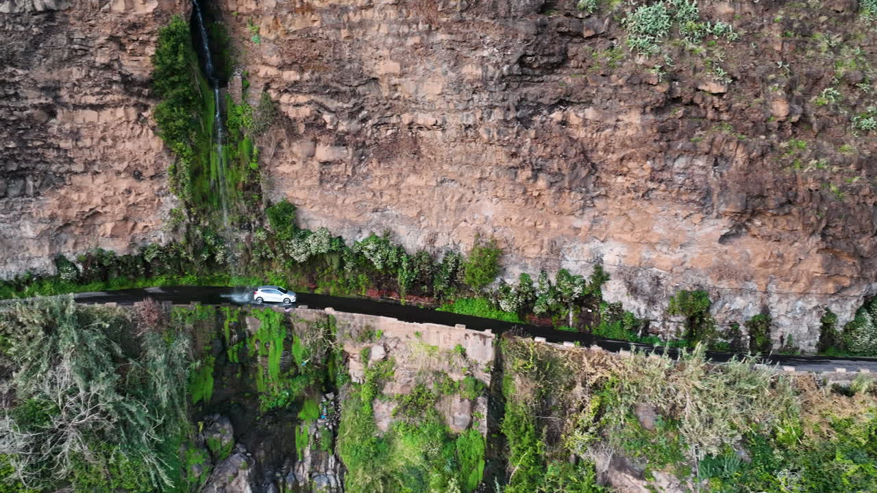 un coche blanco circula bajo la cascada de los ángeles que cae en cascada sobre la carretera junto al acantilado