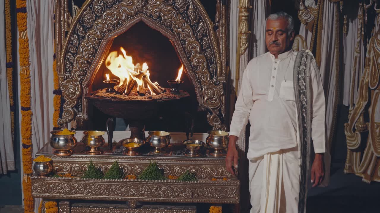 Indian Brahmin priest wearing traditional white clothes performing a Vedic ritual in front of a sacred fire inside a Hindu temple, surrounded by offerings and decorations