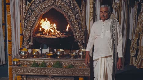 indian brahmin priest wearing traditional white clothes performing a vedic ritual in front of a sacred fire inside a hindu temple, surrounded by offerings and decorations