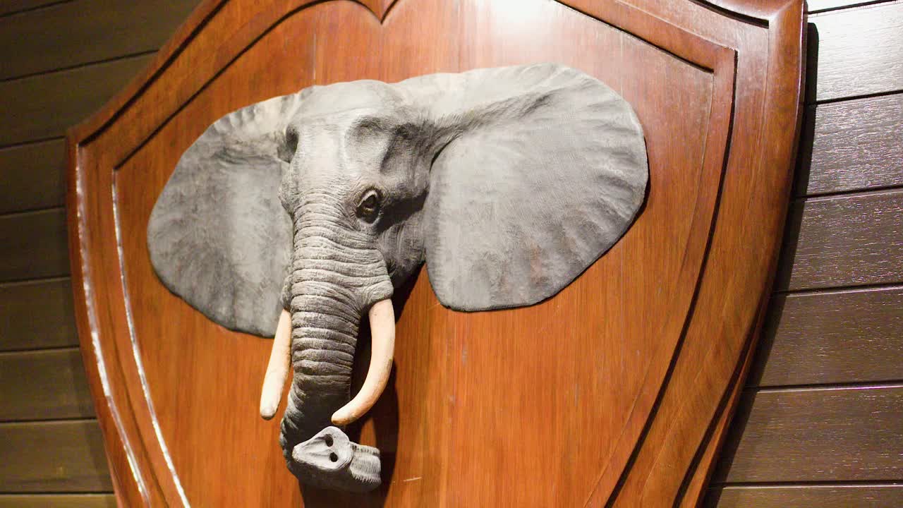 Træelefanthovedskulptur på væg, varm indendørsbelysning, langsomt kamerapanorering, traditionel thailandsk indretning