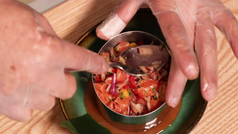 placage de nourriture - chef avec des gants tenant une cuillère et appuyant sur le ceviche de thon sur une plaque en céramique