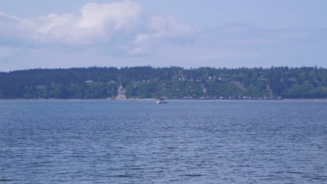 Distant-sailboat-motoring-past-beach-at-Camano-Island-State-Park,-Washington-State-10sec-24fps-slow-motion