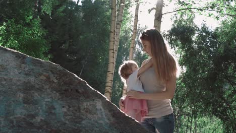 young beautiful mother and daughter playing in the woods near big stone