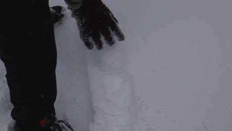 a hand with a glove on is seen rolling a snowball across the ground in slow-motion